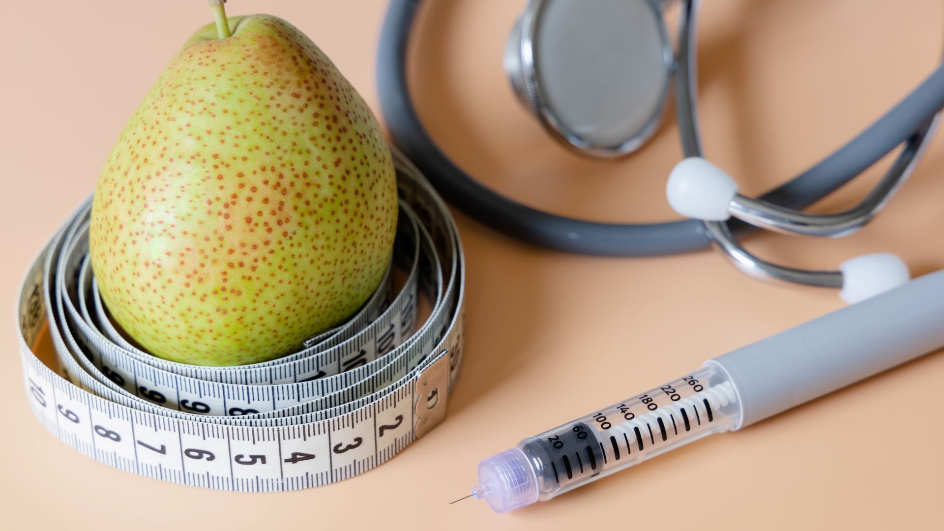 A fresh pear wrapped in a measuring tape, with a syringe and a stethoscope nearby, symbolising health, nutrition, and weight management.