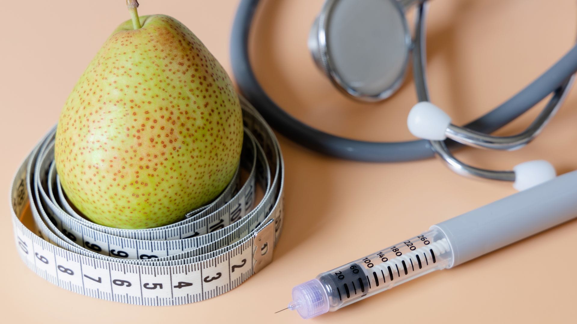 A pear wrapped in a measuring tape, with a syringe and stethoscope on a table.