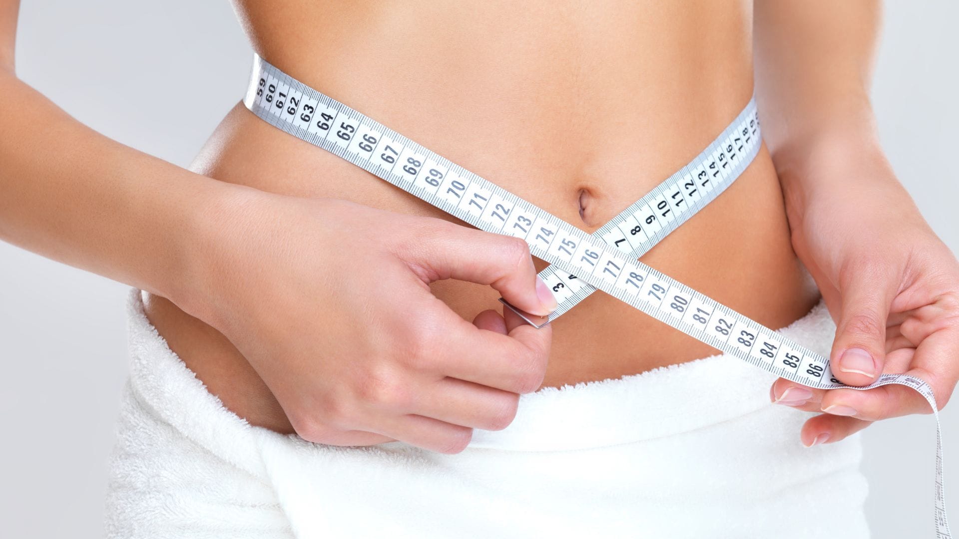 A close-up of a woman measuring her waist with a tape measure.