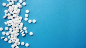 Scattered white round tablets on a bright blue background, illustrating pharmaceutical medication or supplements.