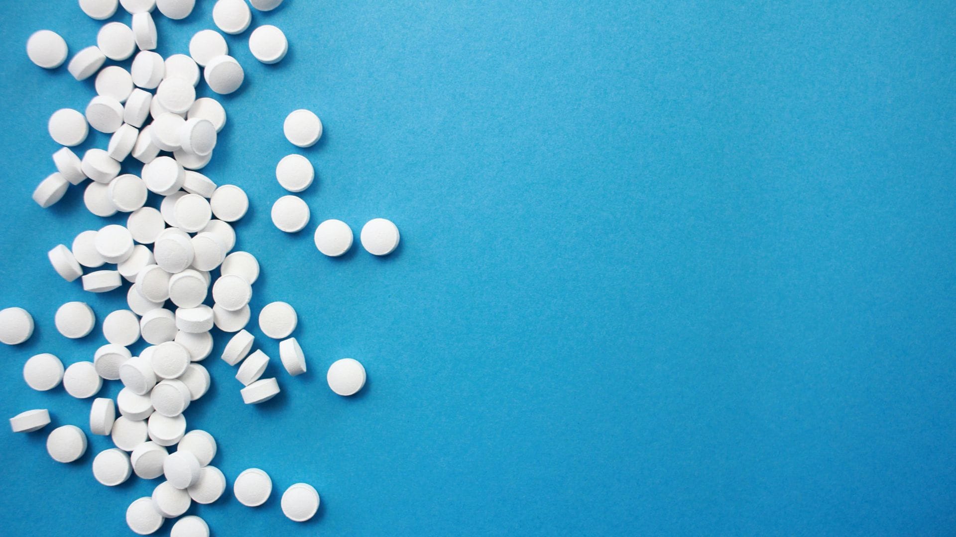 Scattered white round tablets on a bright blue background, illustrating pharmaceutical medication or supplements.