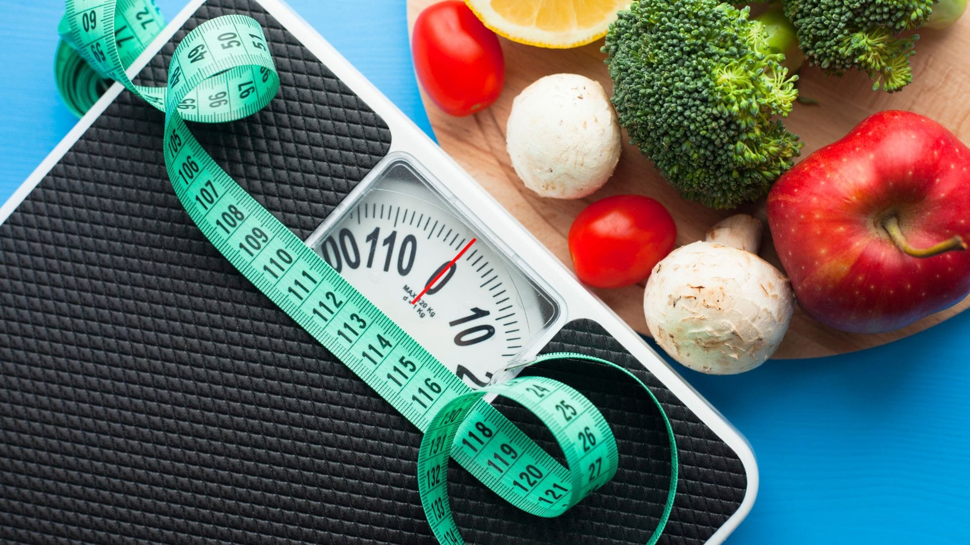 Measuring body weight and healthy food choices with a weighing scale, tape measure, and fresh produce.