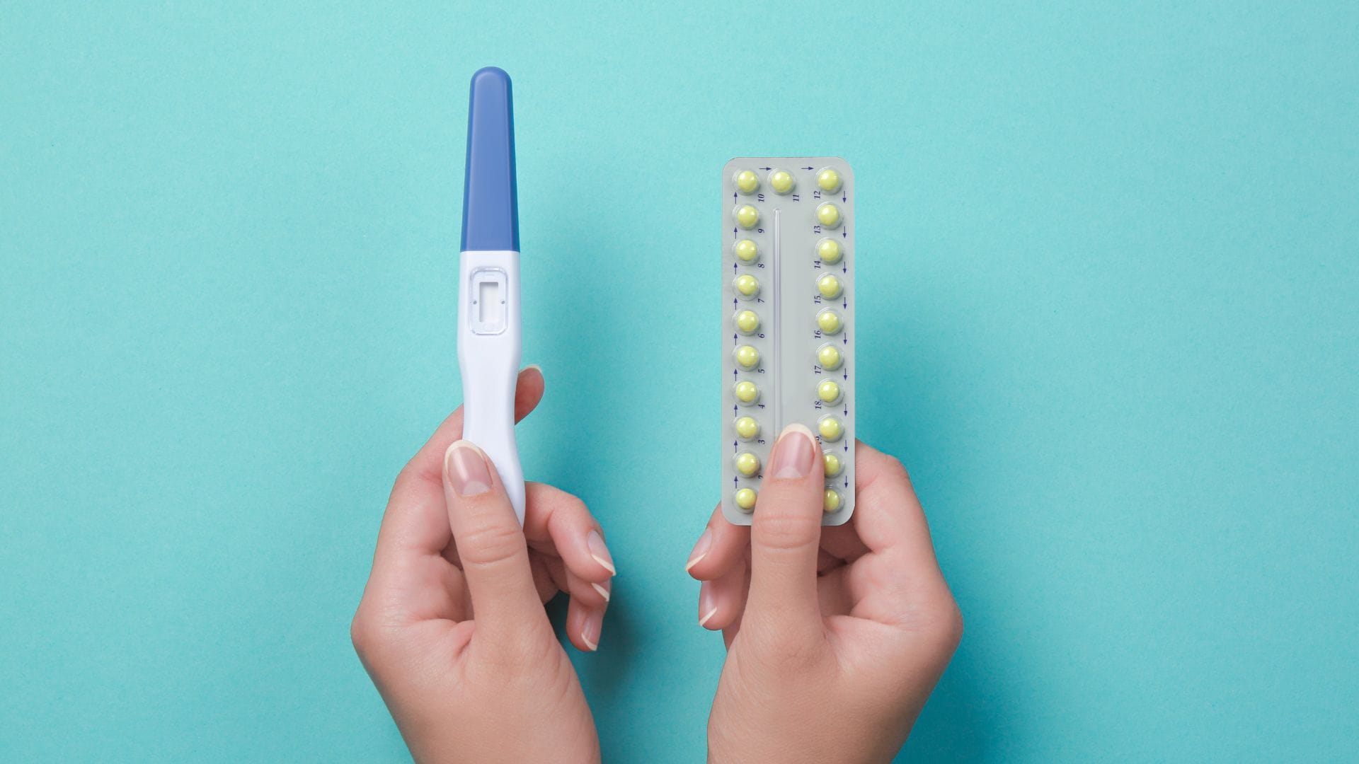 Close-up of hands holding a negative pregnancy test and a blister pack of birth control pills against a teal background.