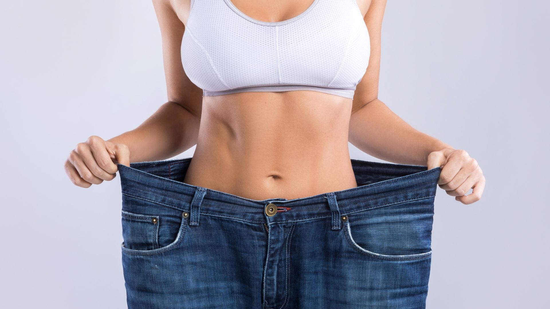 A person in oversized jeans pulling the waistband to show weight loss.