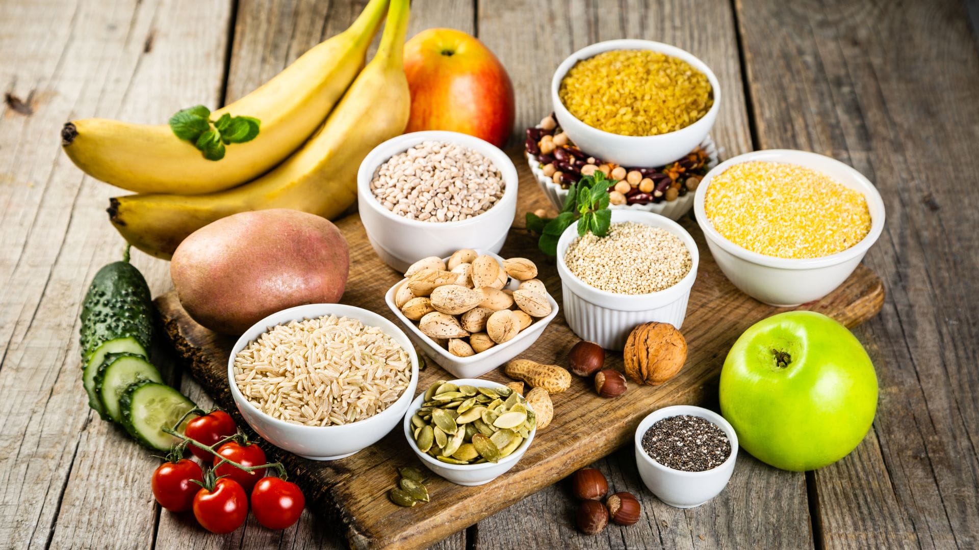Assortment of whole grains, legumes, and fruits on a wooden table representing a balanced diet.