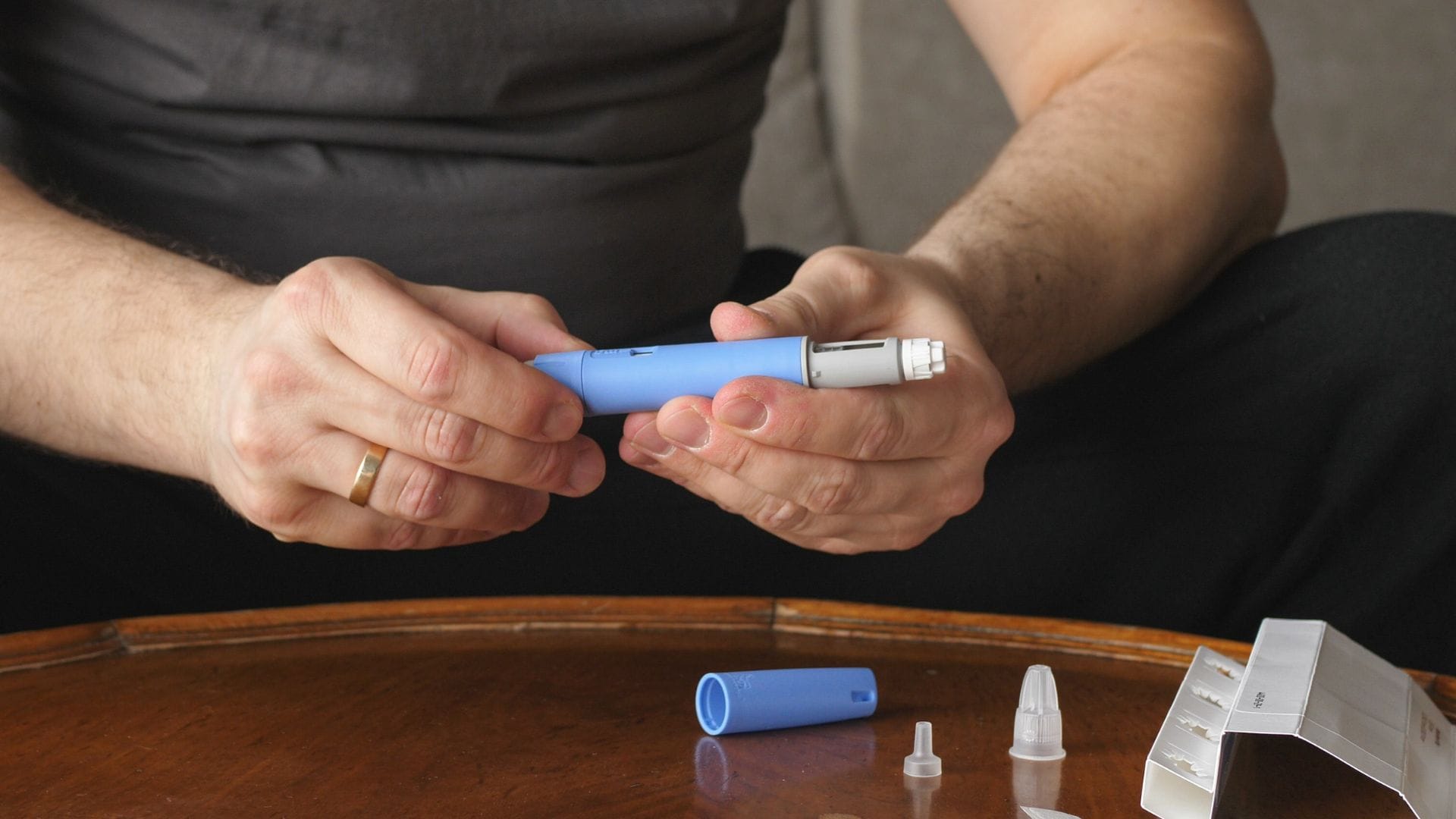 A man holding a blue weight loss injection pen, sitting at a table.