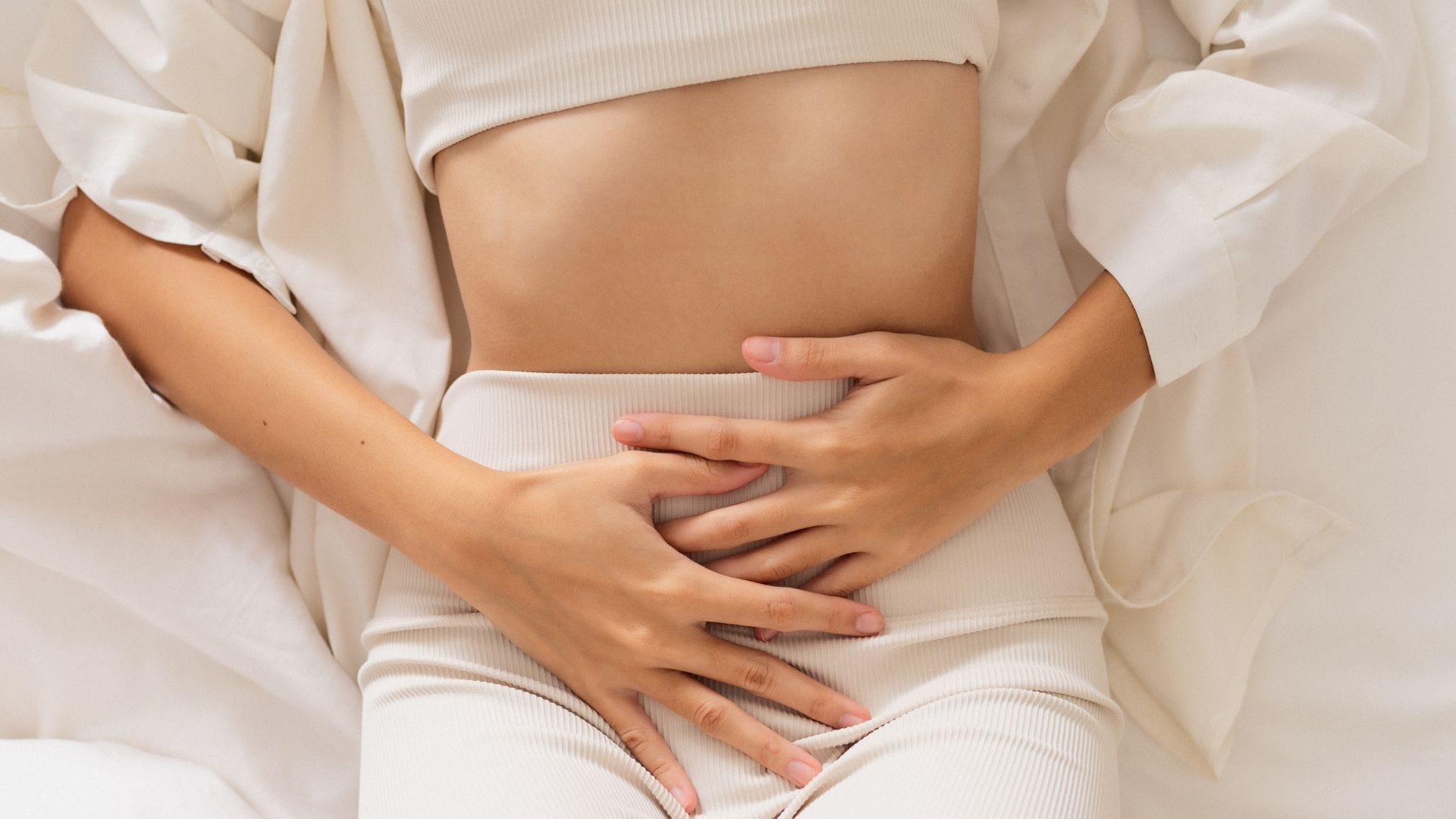 Close-up of a woman's stomach with hands placed over it in pain.
