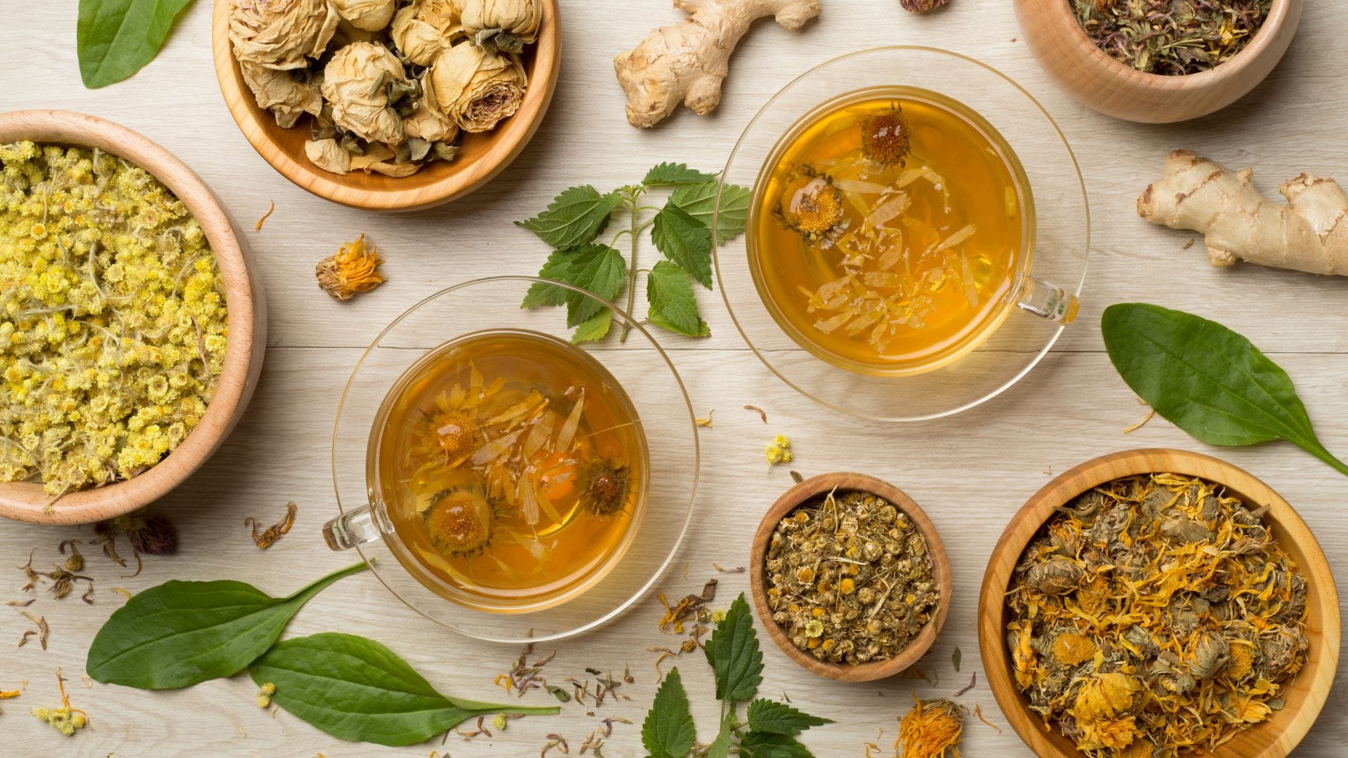 A top view of various herbal teas, dried flowers, and fresh leaves in wooden bowls.