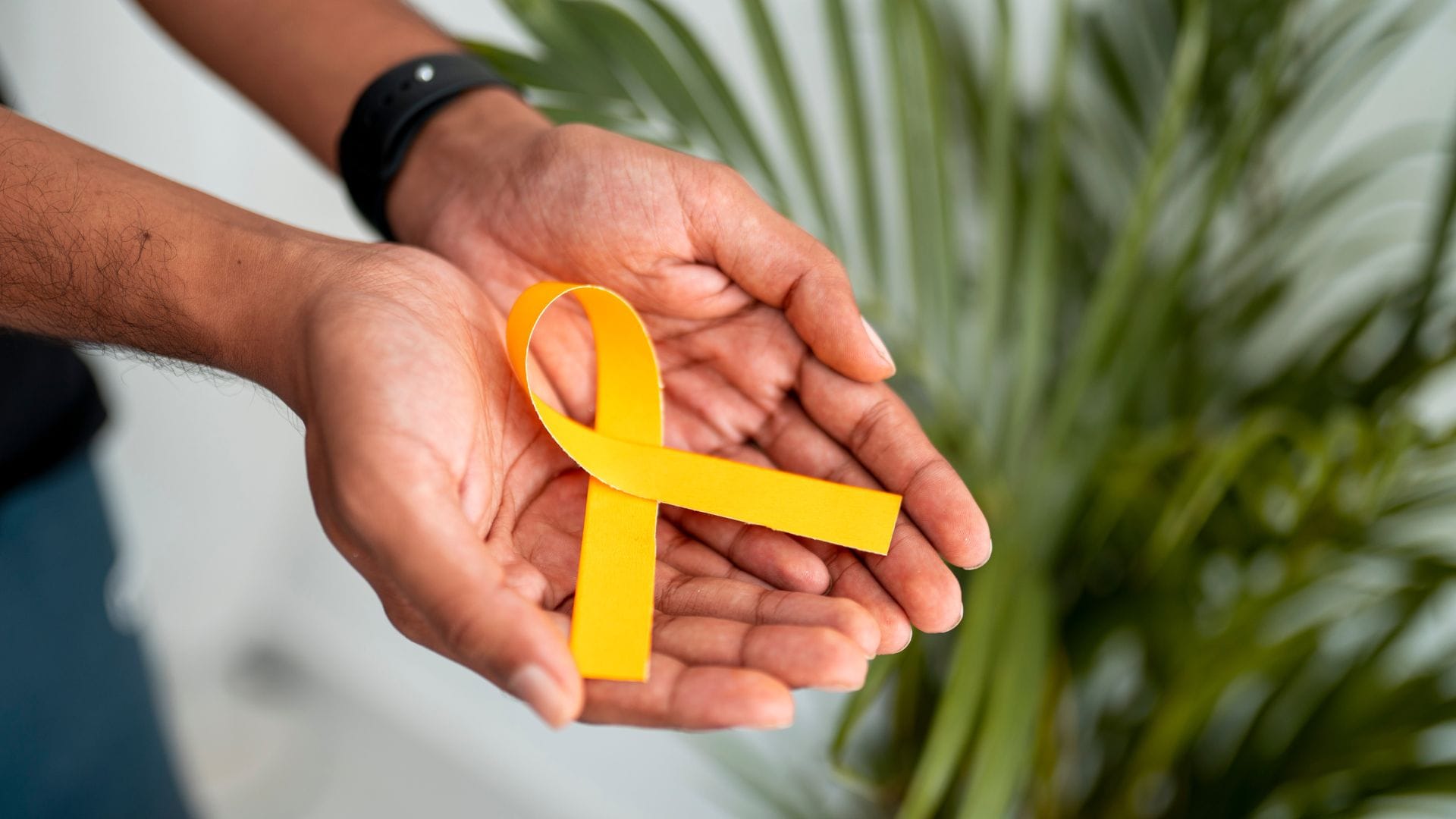 Hands holding a yellow awareness ribbon, symbolising support.