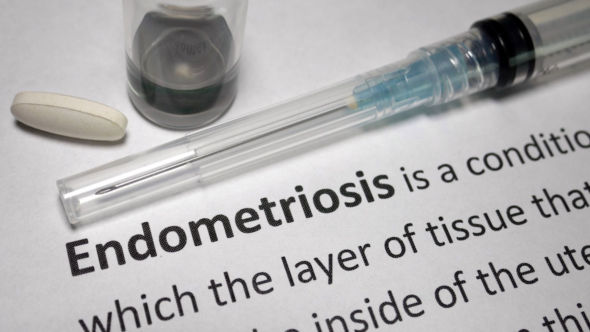 Medical syringe, pill, and vial on a document mentioning endometriosis.
