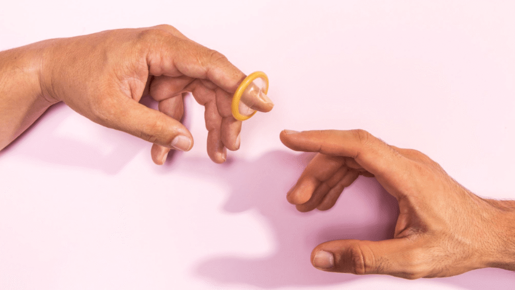 Hands reaching towards each other with a condom stretched over one finger, symbolising safe sex and contraception.