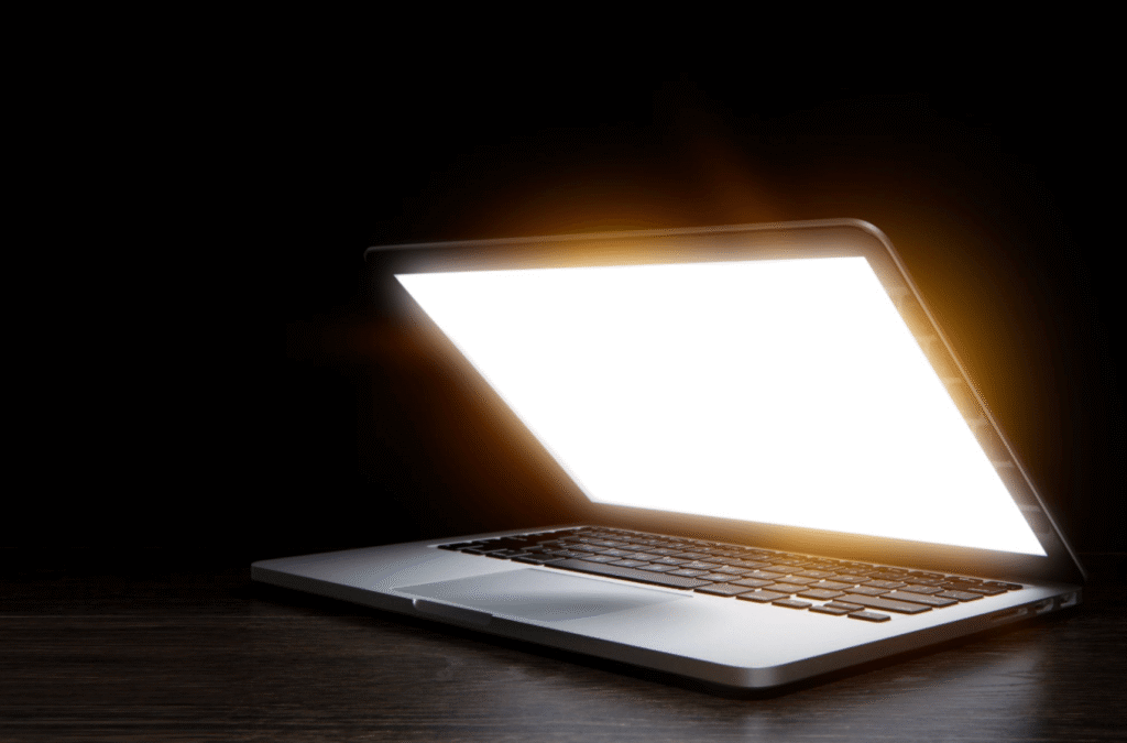 Bright laptop screen glowing in a dark room, illustrating why reducing screen exposure can help during a migraine attack.