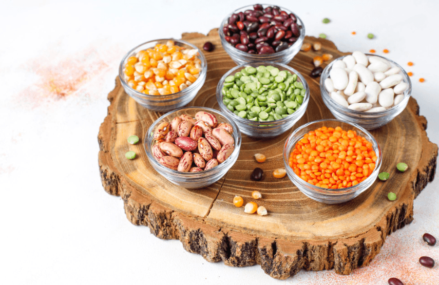 Selection of beans, lentils and pulses in glass bowls on a wooden board, highlighting nutritious plant-based protein sources.