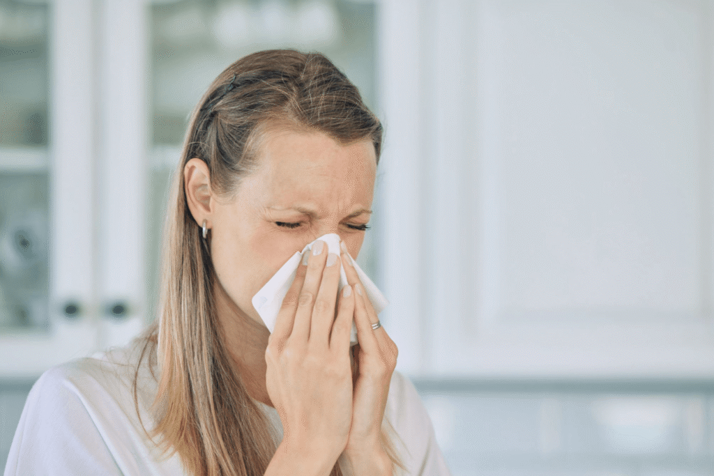 Woman blowing her nose with a tissue while experiencing hay fever symptoms indoors.