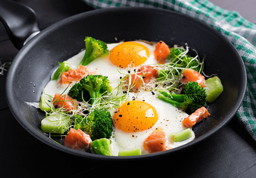 Fried eggs with salmon, broccoli and avocado in a pan, illustrating a protein-rich breakfast that helps keep you full.