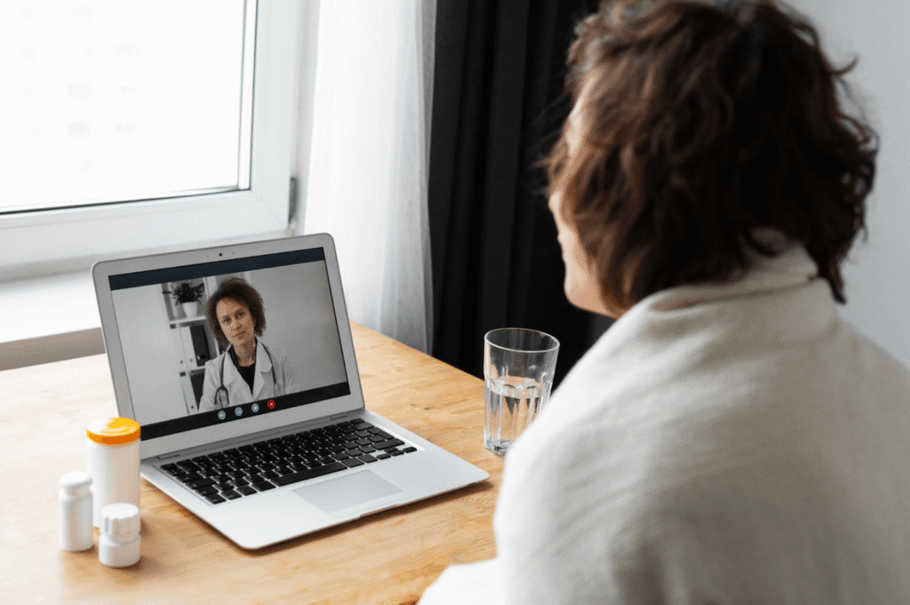 Patient having a virtual doctor appointment on a laptop from home with medication nearby.