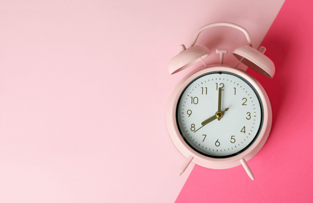 Pink alarm clock on a pink background representing timing, scheduling and period delay treatment planning.