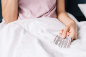 Person sitting in bed holding a blister pack of the morning after pill on white bedding.
