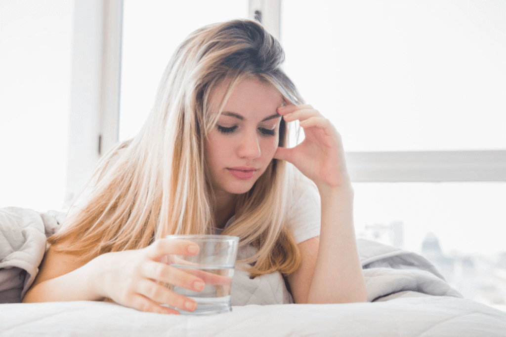 Woman resting in bed with a glass of water, illustrating possible side effects and safety considerations of migraine medication.