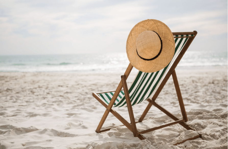 Empty beach chair with a sun hat facing the sea, representing travel preparations and ordering medication before a holiday.