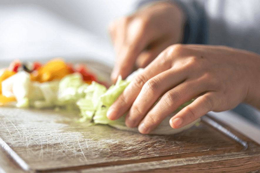 Person chopping fresh vegetables on a wooden chopping board, preparing a healthy meal with filling whole foods.
