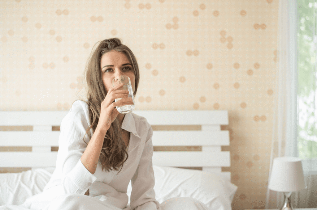 Person sitting on a bed drinking water before or after taking the morning after pill.