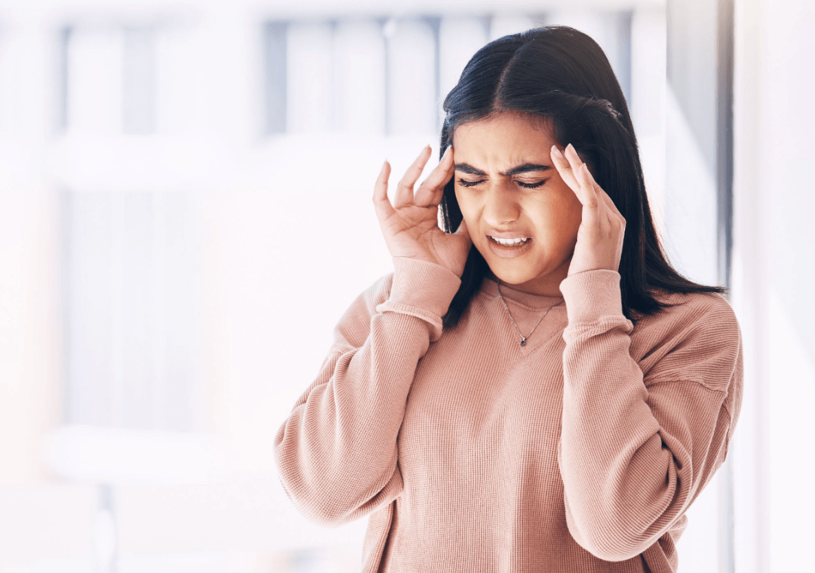 Woman holding both sides of her head while experiencing migraine pain.
