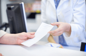 Pharmacist handing a prescription to a patient at a pharmacy counter, representing prescription migraine medication.