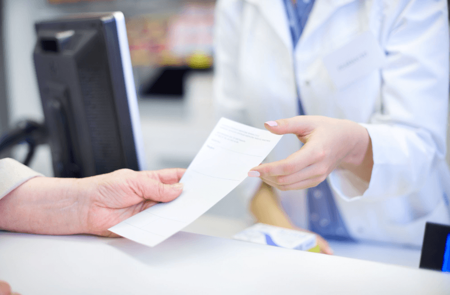 Pharmacist handing a prescription to a patient at a pharmacy counter, representing prescription migraine medication.