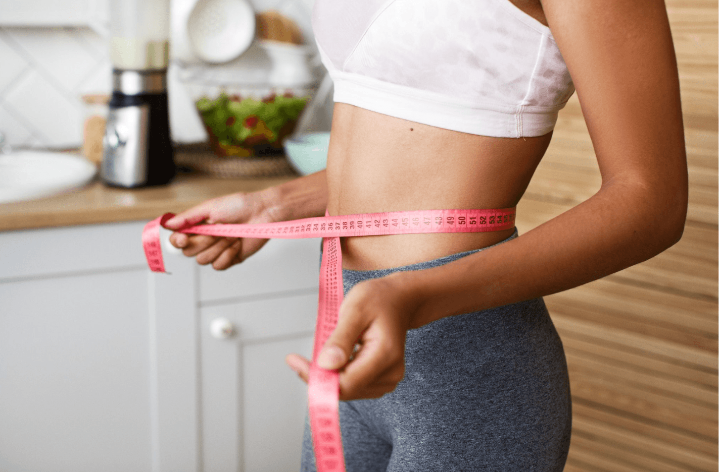 Woman measuring her waist with a tape measure while following a weight loss journey at home.