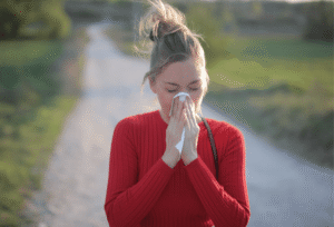 Woman outdoors blowing her nose into a tissue during allergy season, showing why hay fever can feel worse in some years.