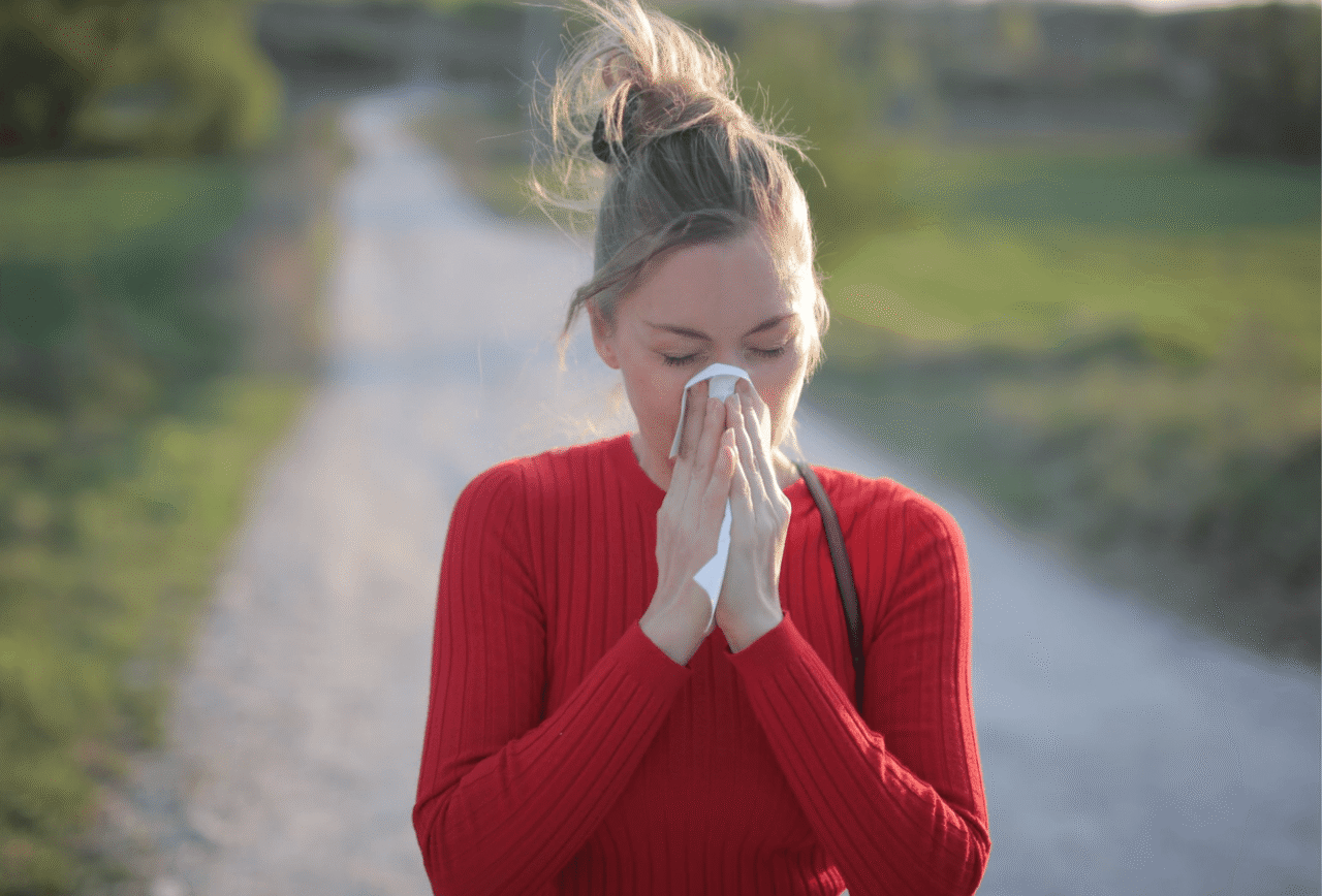 Woman outdoors blowing her nose into a tissue during allergy season, showing why hay fever can feel worse in some years.