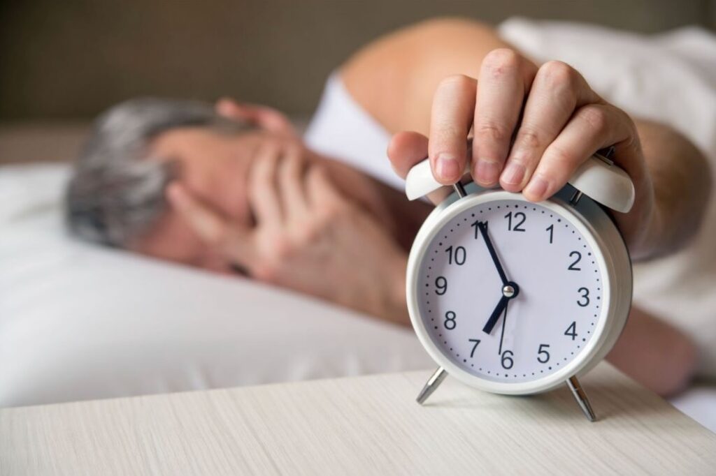 Tired man reaching for an alarm clock after disrupted sleep