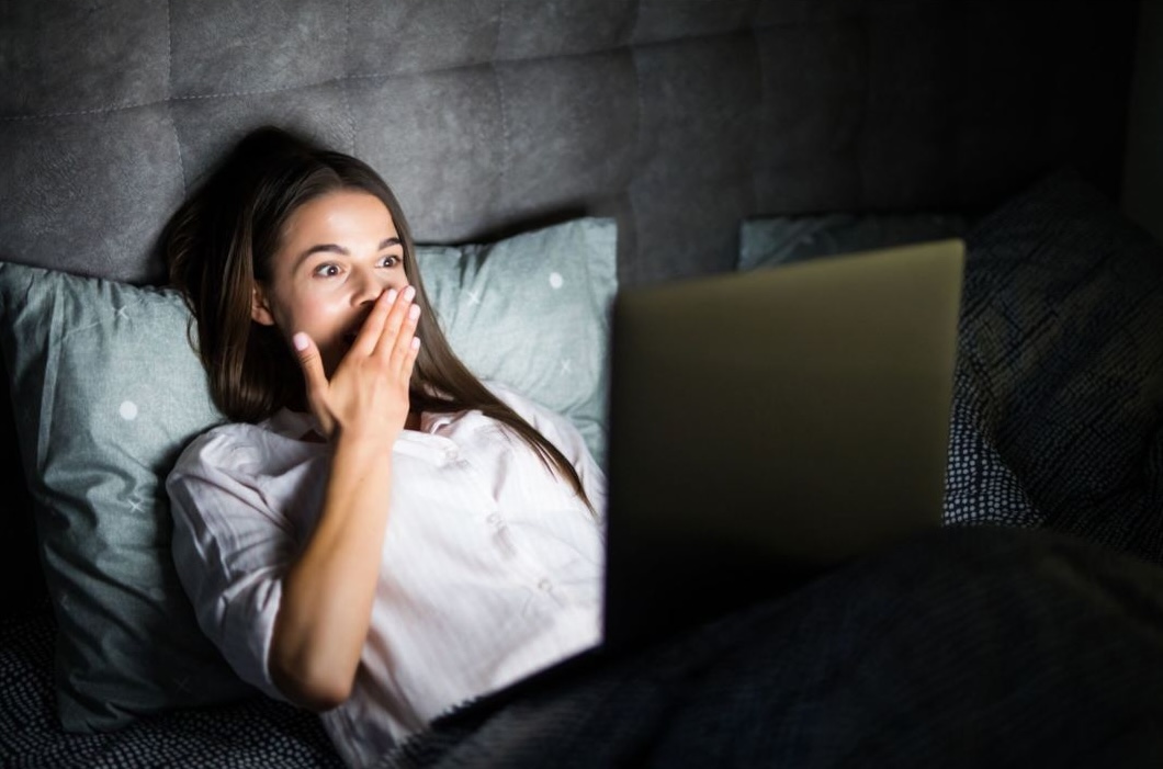 Woman using a laptop in bed at night while feeling tired